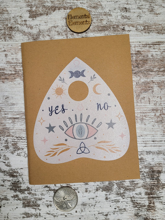 Planchette journal with triple moon goddess, the moon and sun, an evil eye, stars, and leaves.