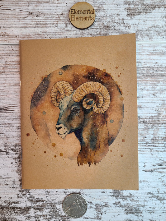 Aries Zodiac journal shows the side view of the head of a ram in shades of browns and blues. Aries has a brown and blue watercolor circle background.