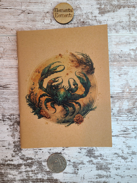 Cancer zodiac astrology journal shows a water color depiction of a large blue and brown crab within a brown, tan, and blue circle that has reef and floral elements surround.