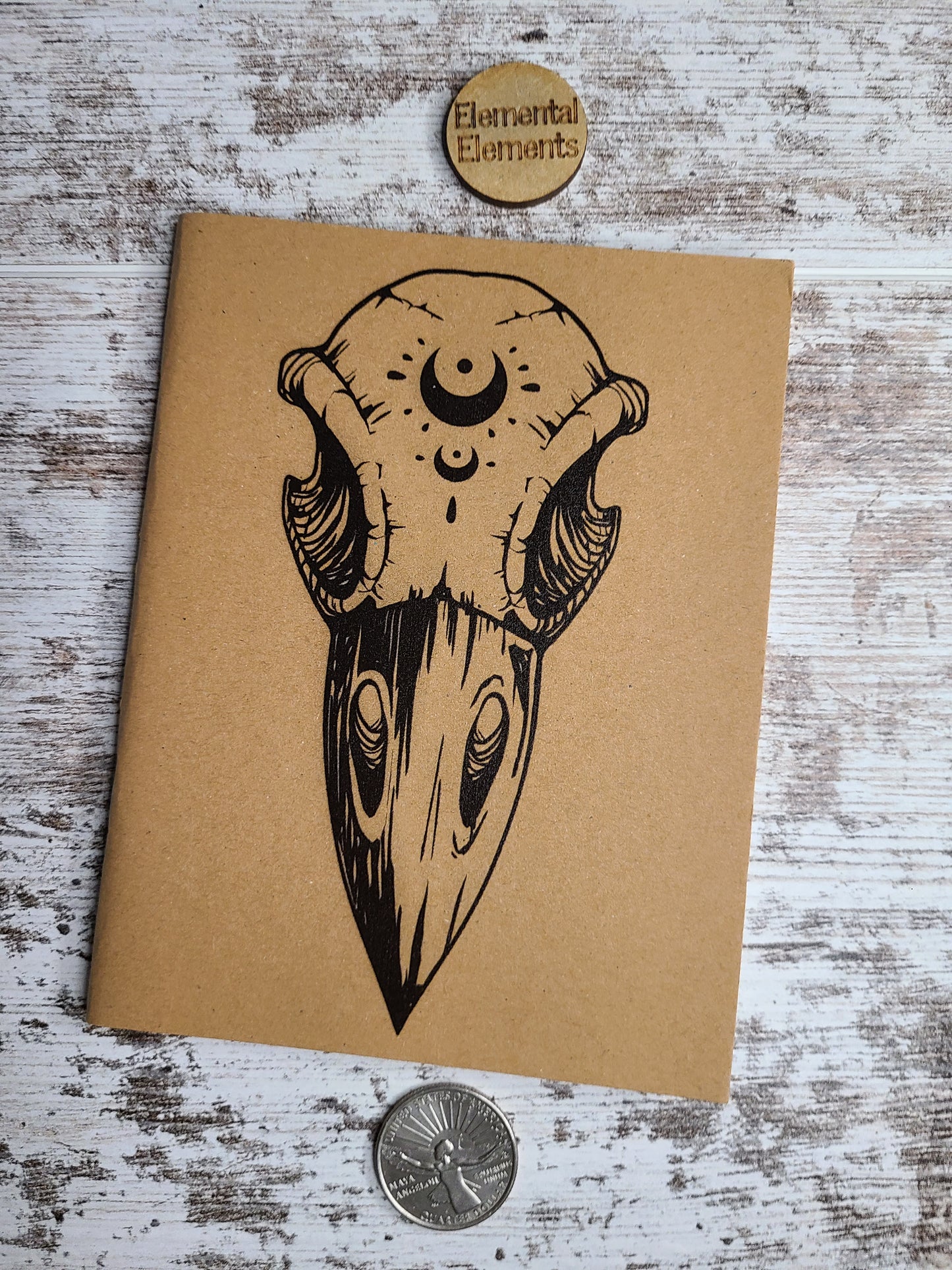 Journal with art of the front view of a raven skull with two crescent moons on the forehead.