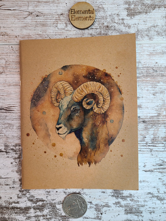 Aries Zodiac journal shows the side view of the head of a ram in shades of browns and blues. Aries has a brown and blue watercolor circle background. 