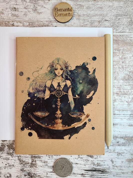 Libra human with long green and purple ombre hair. Gold balance scales in front of them with green, black, and blue smoke and stars in the background. Journal is sitting on top of an open journal showing blank pages. An eco-friendly pen lies next to the Zodiac journal.