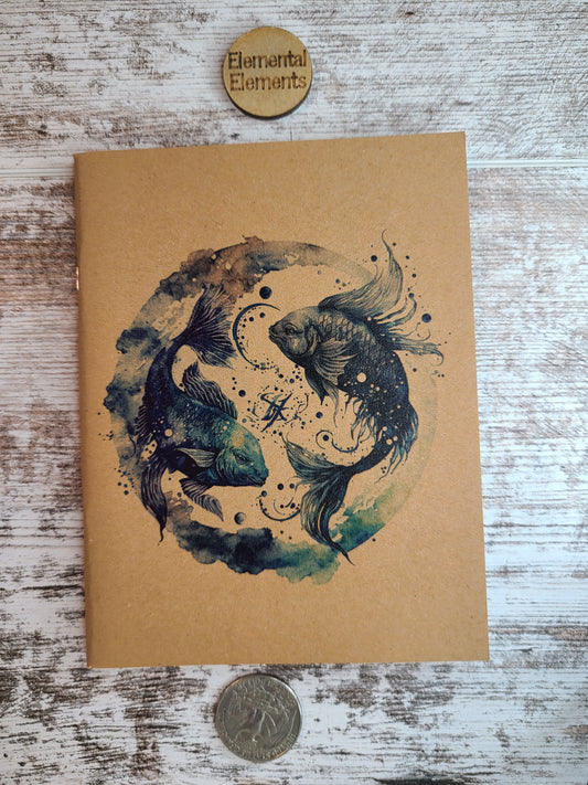 Pisces zodiac journal two beta koi fish opposite each other within a watercolor circle of blues, browns, and greens.